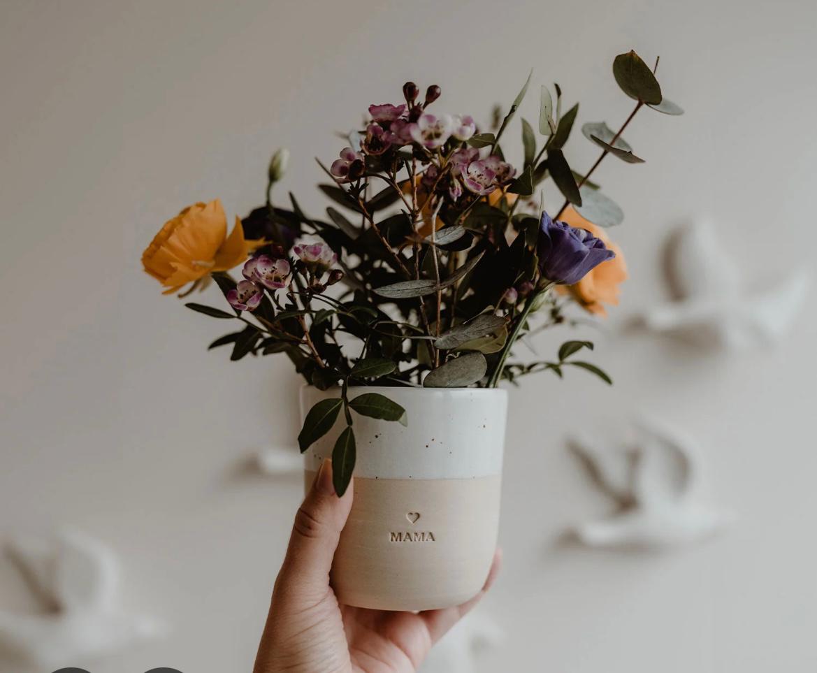 Hand hält eine Keramikvase mit buntem Blumenstrauß