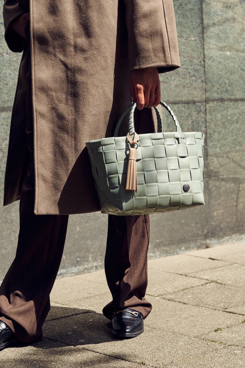 Person mit hellgrüner geflochtener Tasche